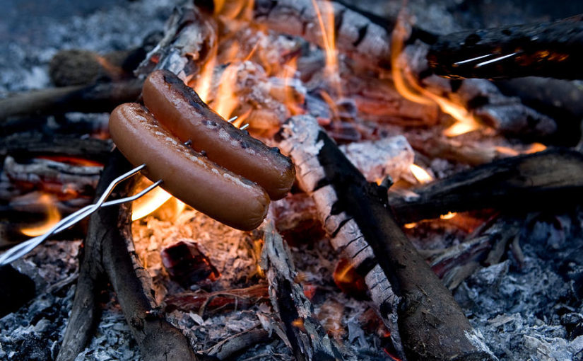 Cooking hotdogs over a campfire.