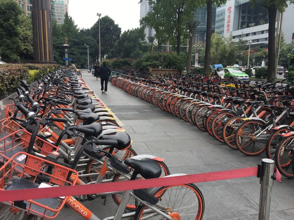 Bicycle deposits like this one are everywhere. Each ride has an electronic gizz which that lets you rent it using–what else?–WeChat. The system is not robustly communistlc: Different companies paint their bikes in different colors, and have sales to compete. Phredfoto.