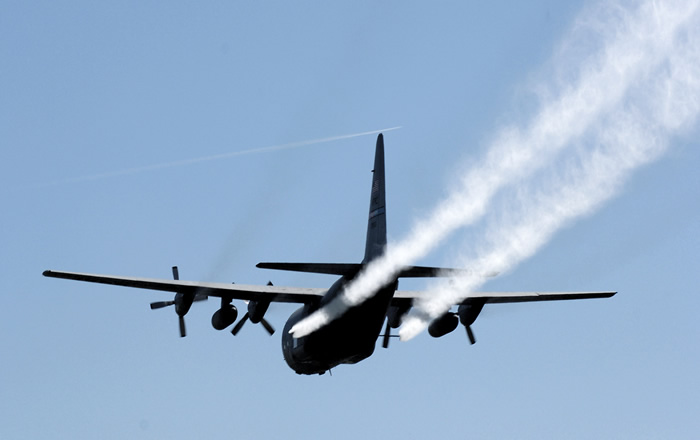 An American Air Force C-130 spraying pesticides over a target area.